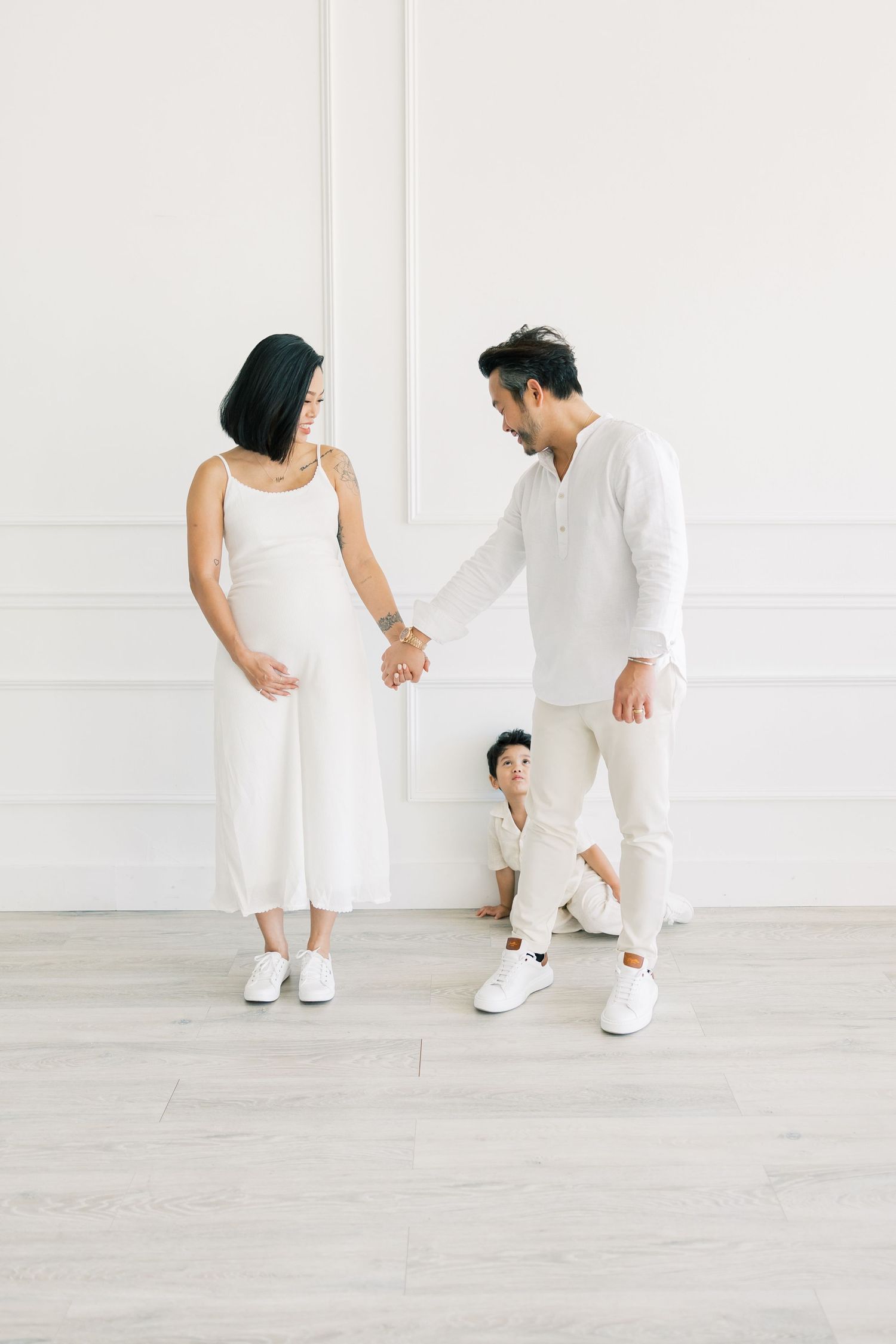 A family in coordinated white outfits shares a playful moment together in a bright studio setting.