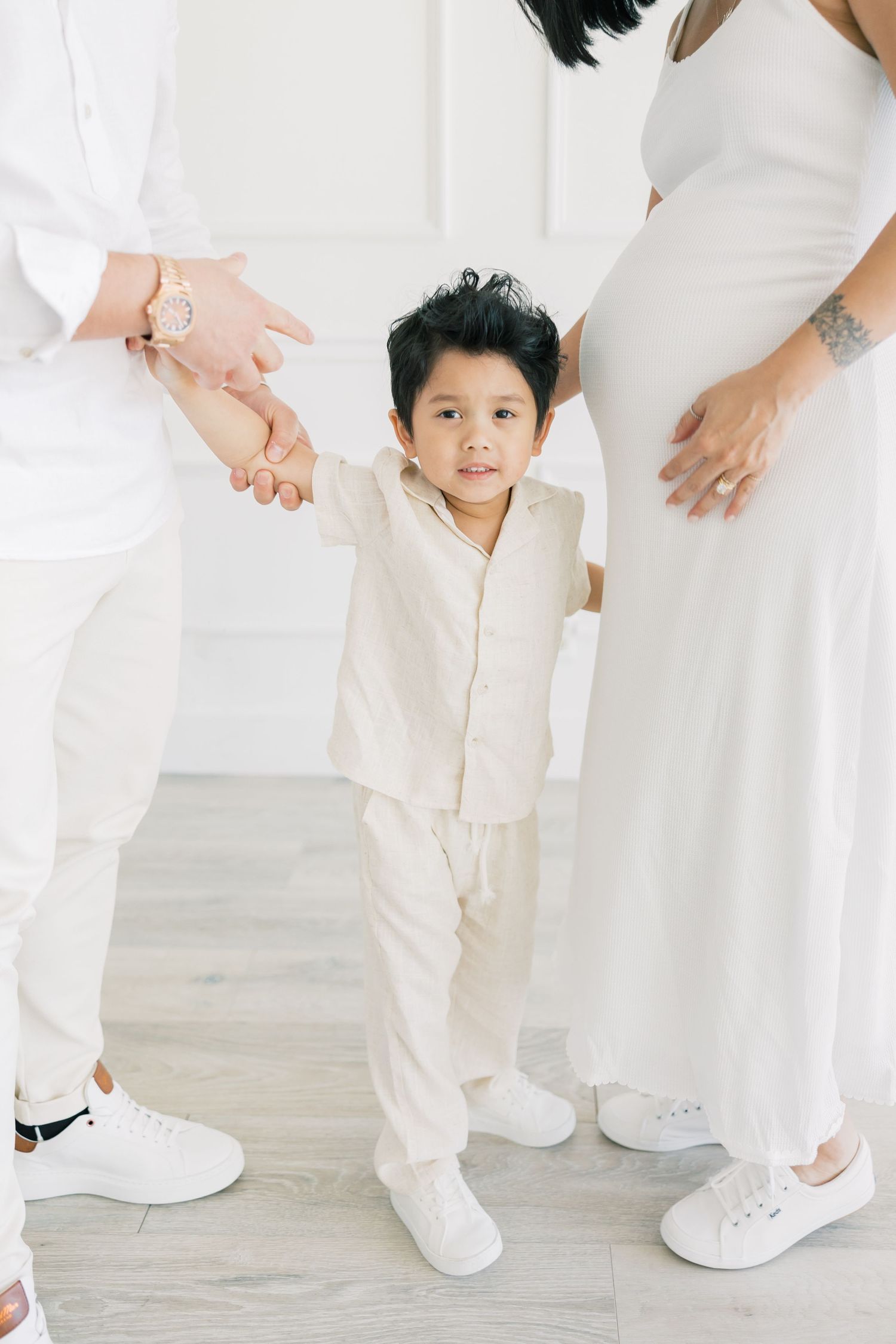A young child stands between two people wearing all white outfits and matching white sneakers.
