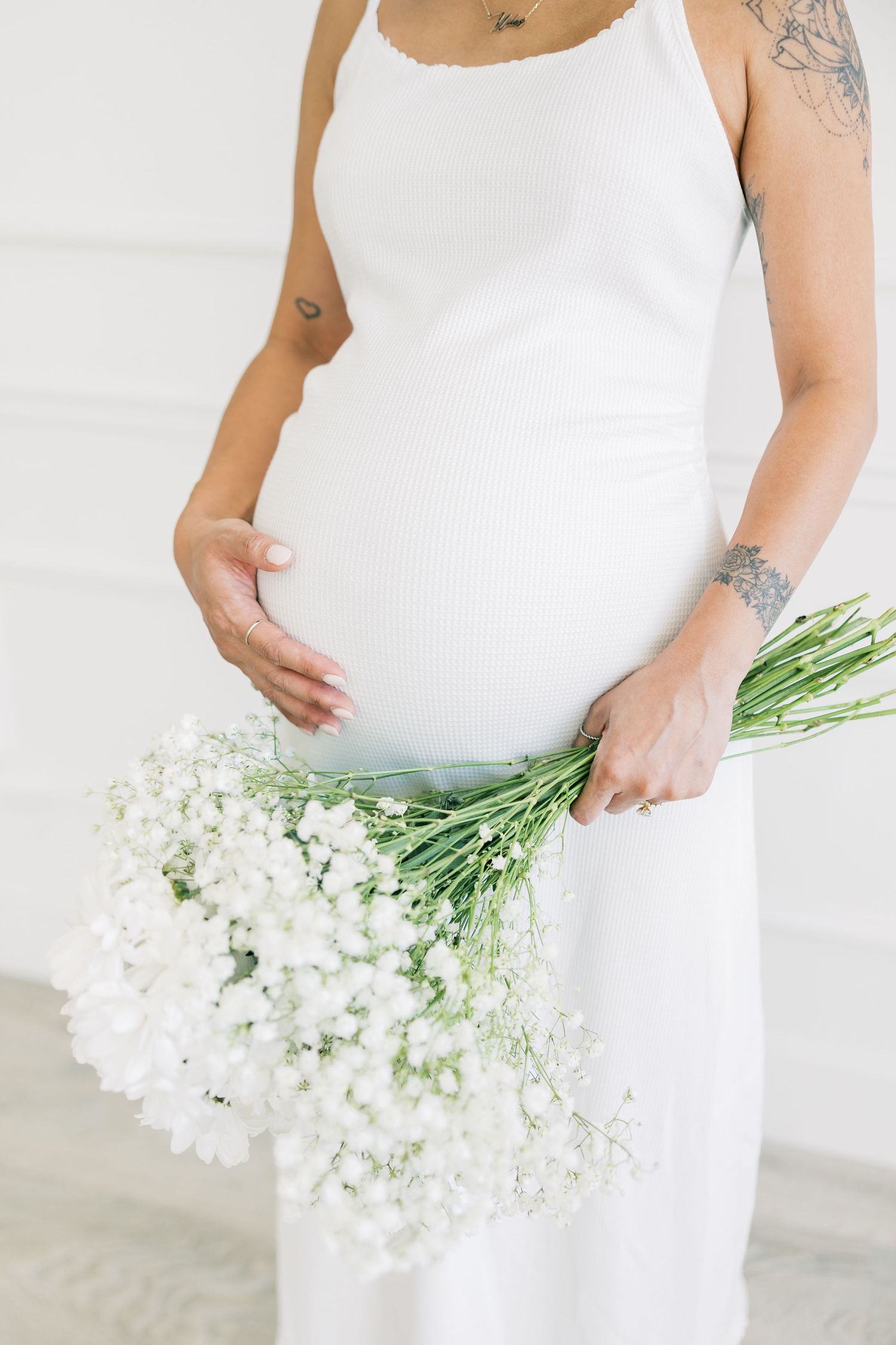 Close up view of a pregnant belly in a white dress with delicate white flowers.
