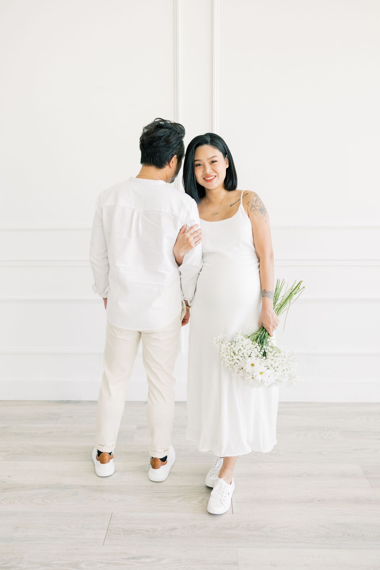 A couple dressed in white share a sweet moment while holding baby's breath flowers.