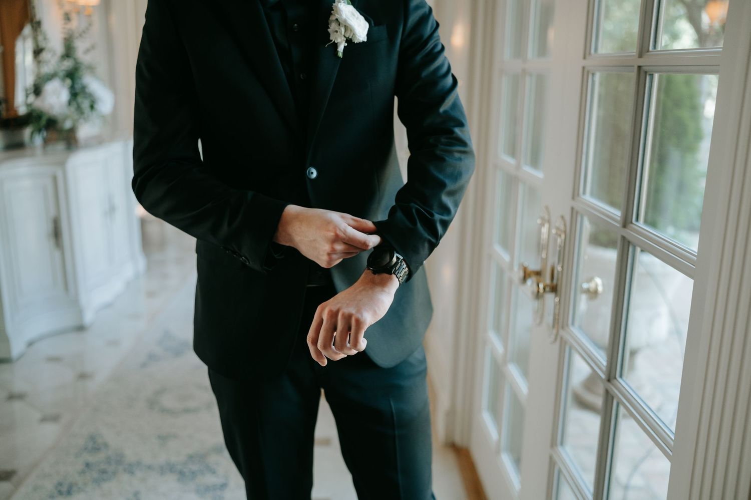A close-up view of a groom adjusting his cufflinks while wearing a classic black suit.