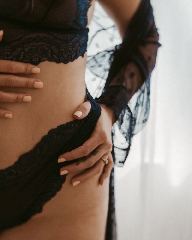 Black and white photo showing a person resting on a bed wearing black lace lingerie, viewed from behind.