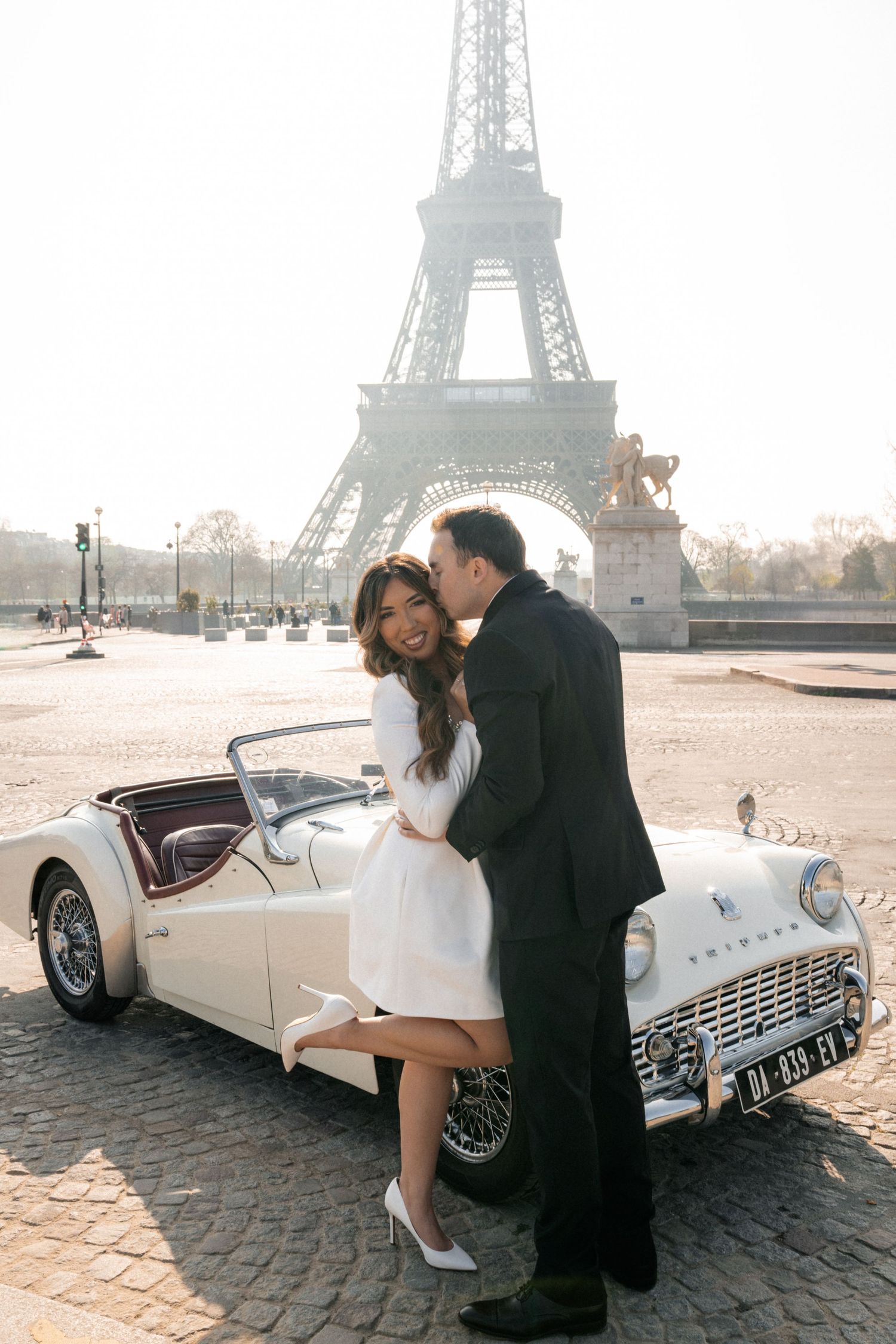 A romantic black and white embrace of a couple at a scenic overlook with cityscape and water views in the background.