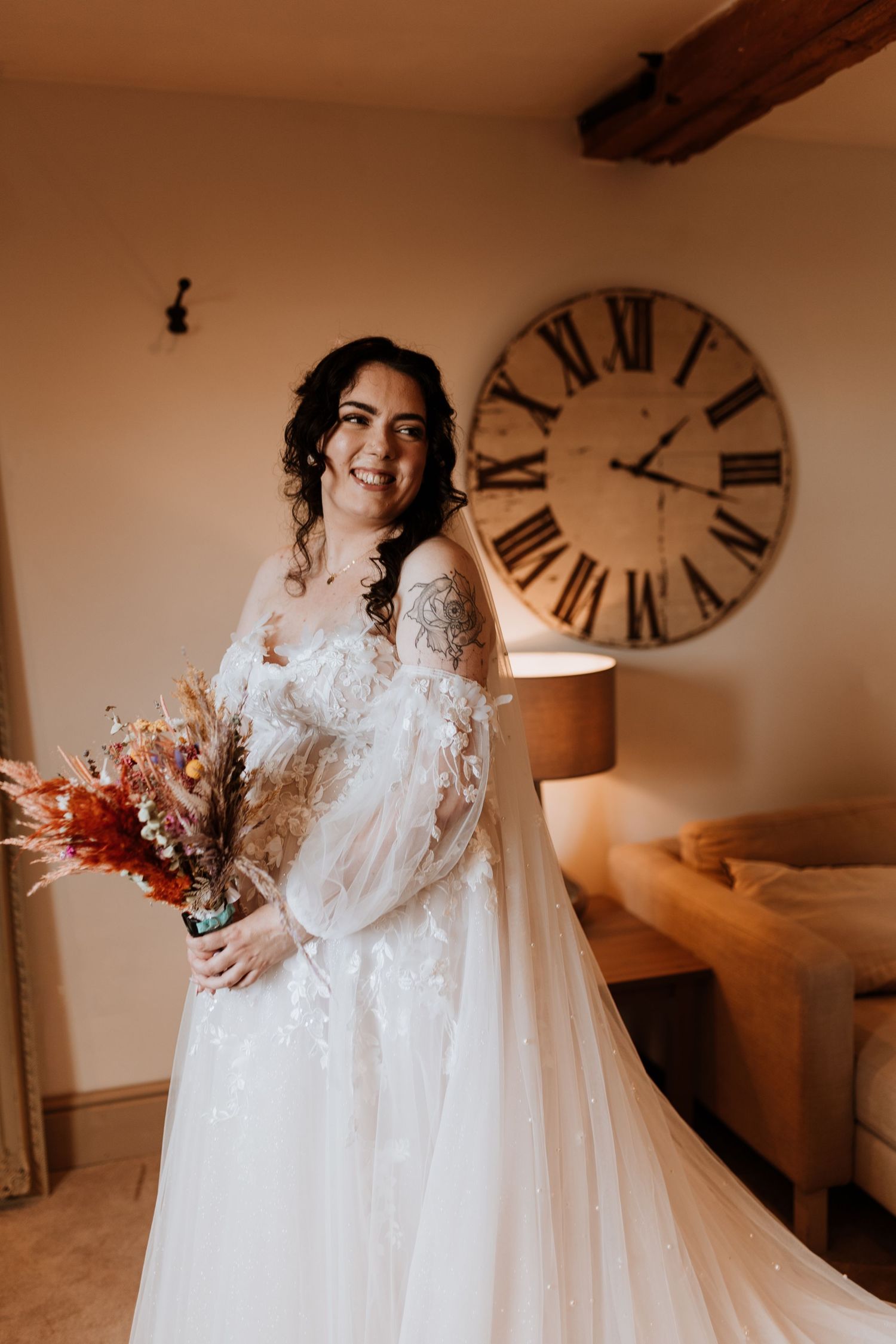 A bride in a flowing white lace gown twirls gracefully in a rustic room with a vintage clock on the wall.
