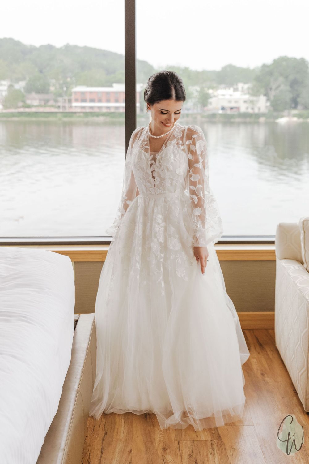 White lace wedding dress with delicate floral details displayed by a waterfront window.