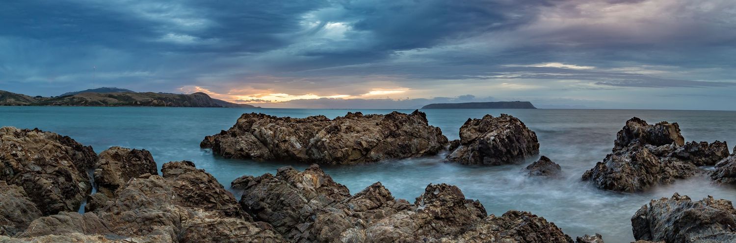 Dramatic coastal seascape with rocky outcrops under moody sunset sky.