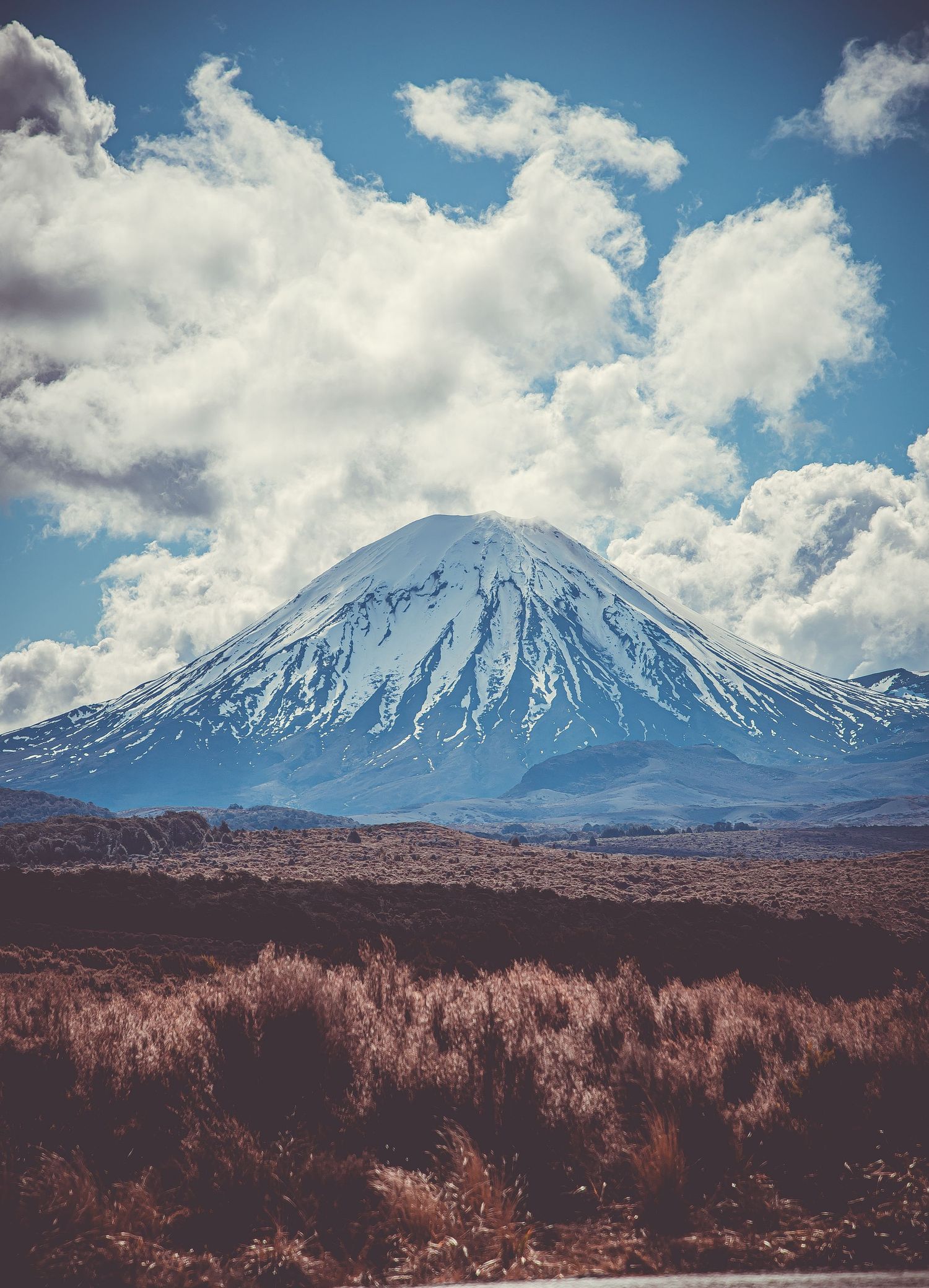 Snow-capped Mount Fuji rises majestically against a blue sky with puffy white clouds.