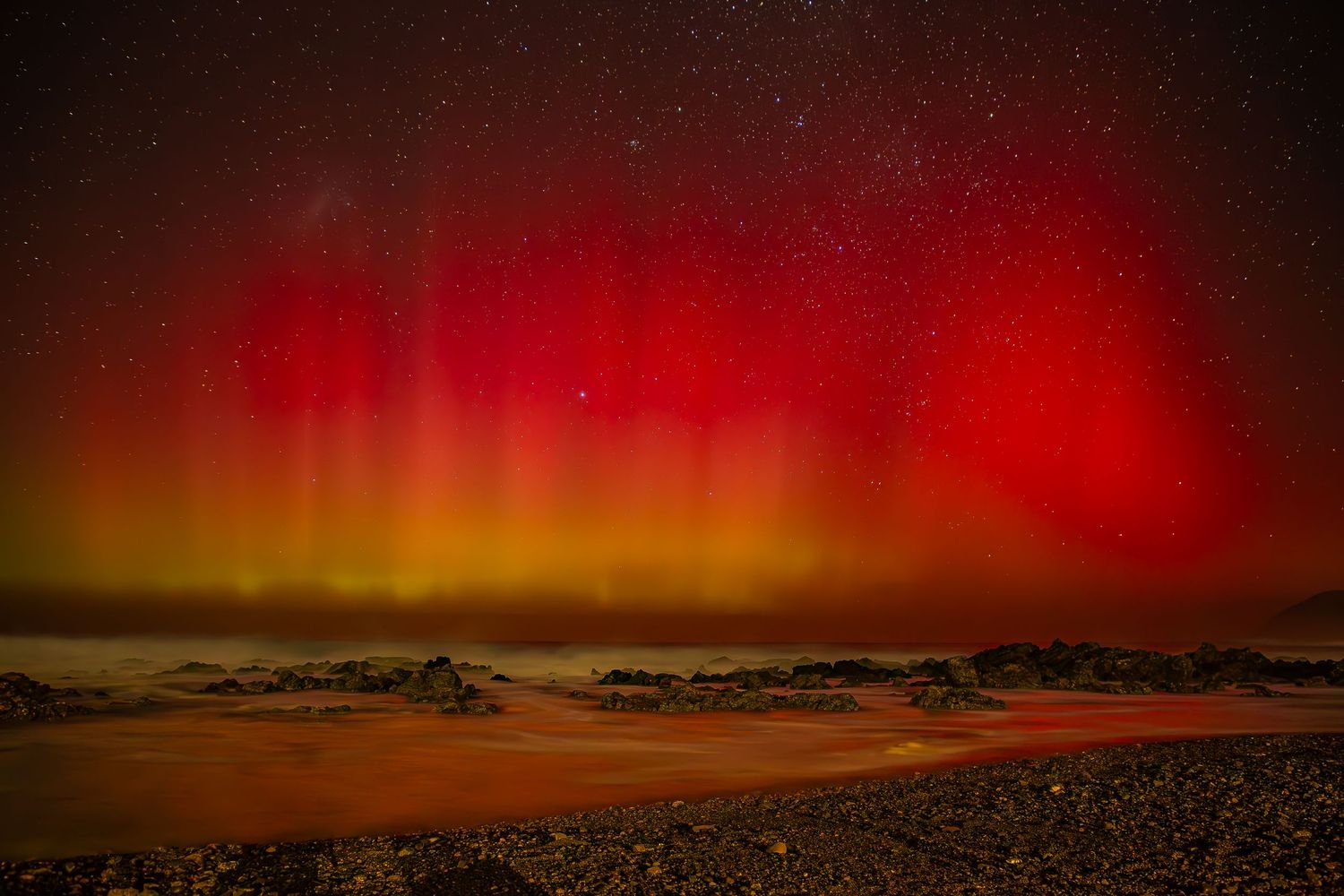 Vibrant red and yellow aurora borealis illuminates night sky over snowy arctic landscape beneath twinkling stars.