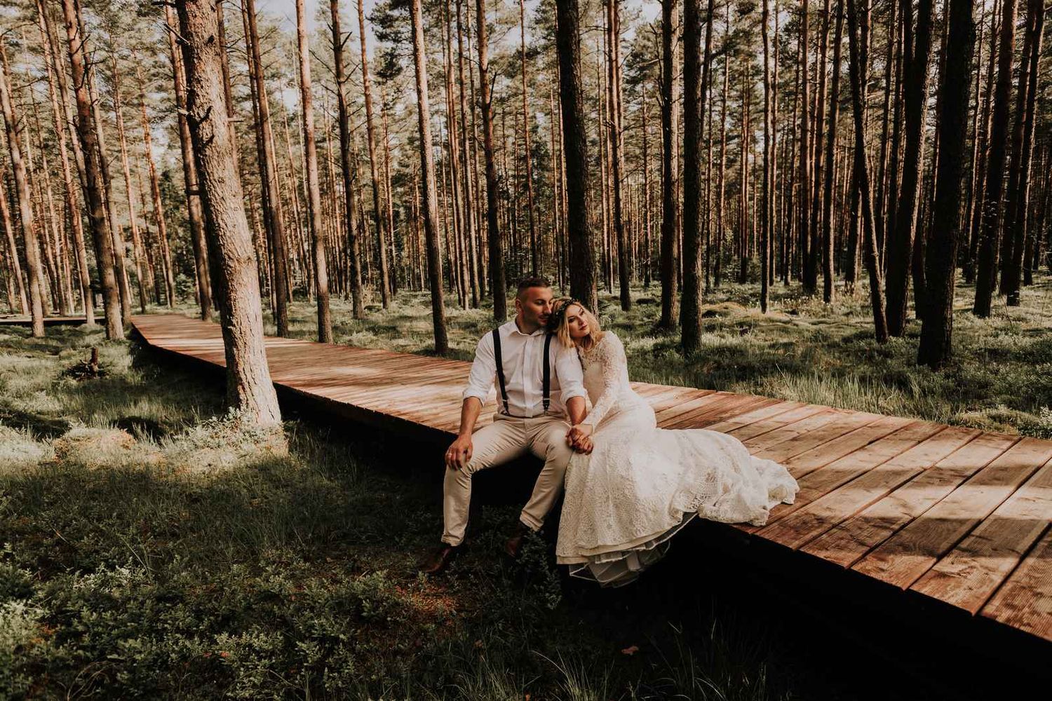 Sesja ślubna na torfowisku - para młoda odpoczywa na drewnianej kładce w lesie
