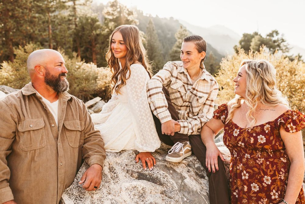 A group sits together outdoors on a sun-lit rock formation wearing casual fall clothing in earth tones and patterns.