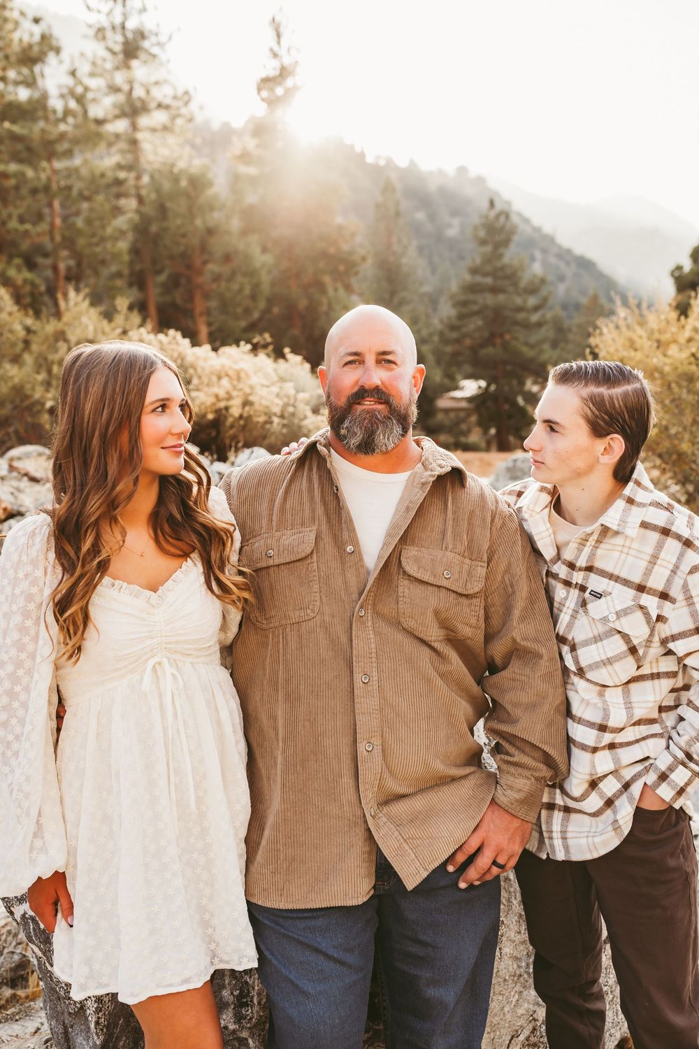 Family group shares candid laughter and loving moments during golden hour photoshoot in mountain setting.