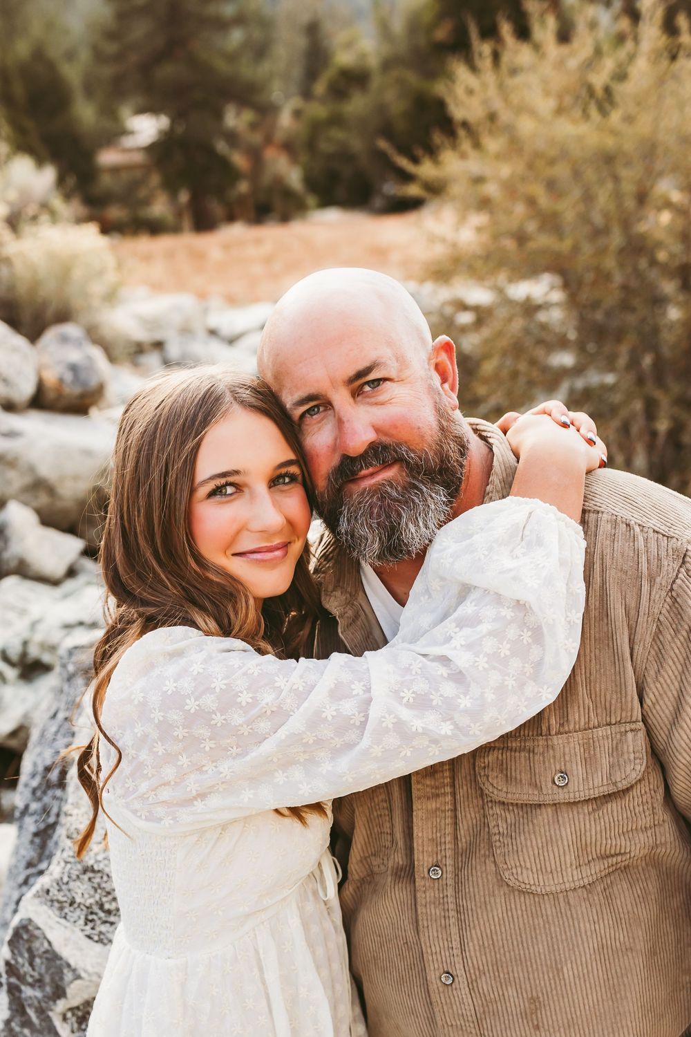 Two people embracing outdoors on an autumn day with trees and rocks in background.