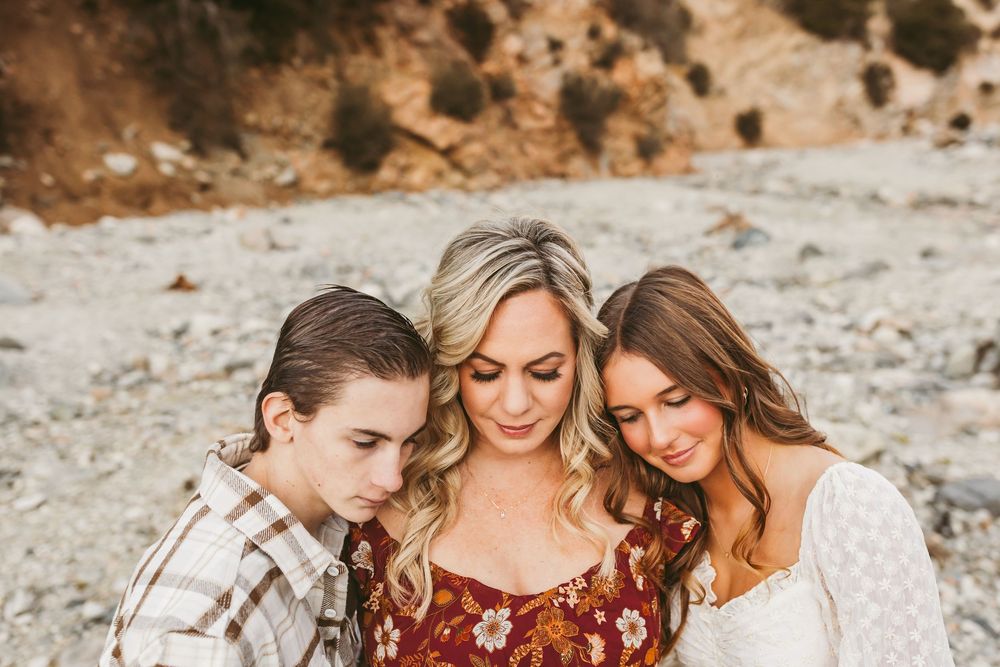 Three people wearing casual attire smiling and looking down together against a rocky outdoor background.
