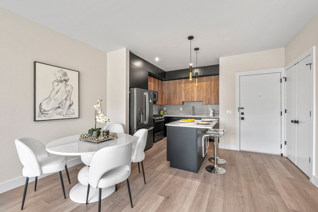 Modern open concept apartment interior featuring hardwood floors, white dining set and kitchen with wood cabinets and gray island.