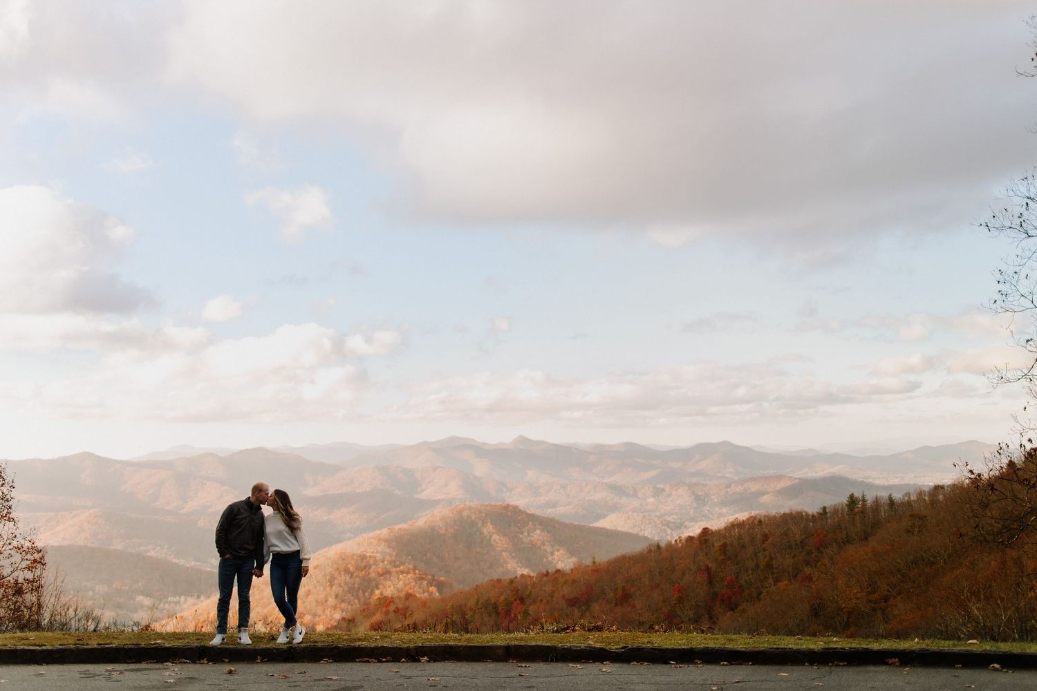 Two silhouettes stand together overlooking a scenic mountain landscape at sunset on the Blue Ridge Parkway.