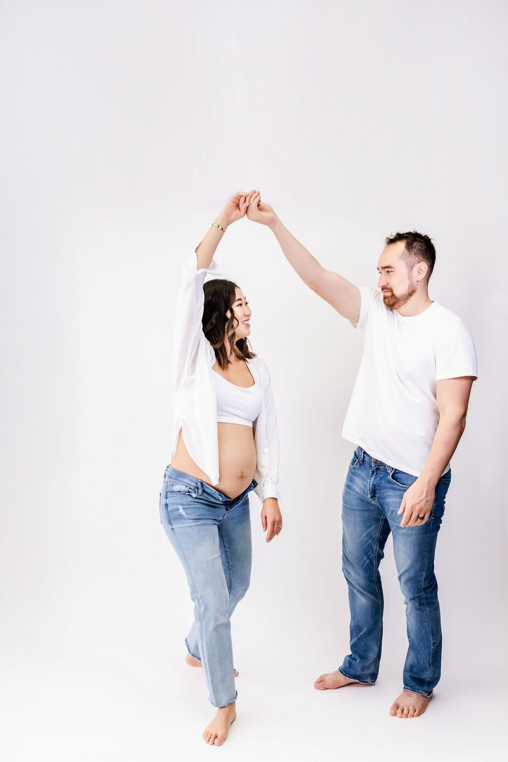 Dancing couple in white and denim against light background showing playful movement.