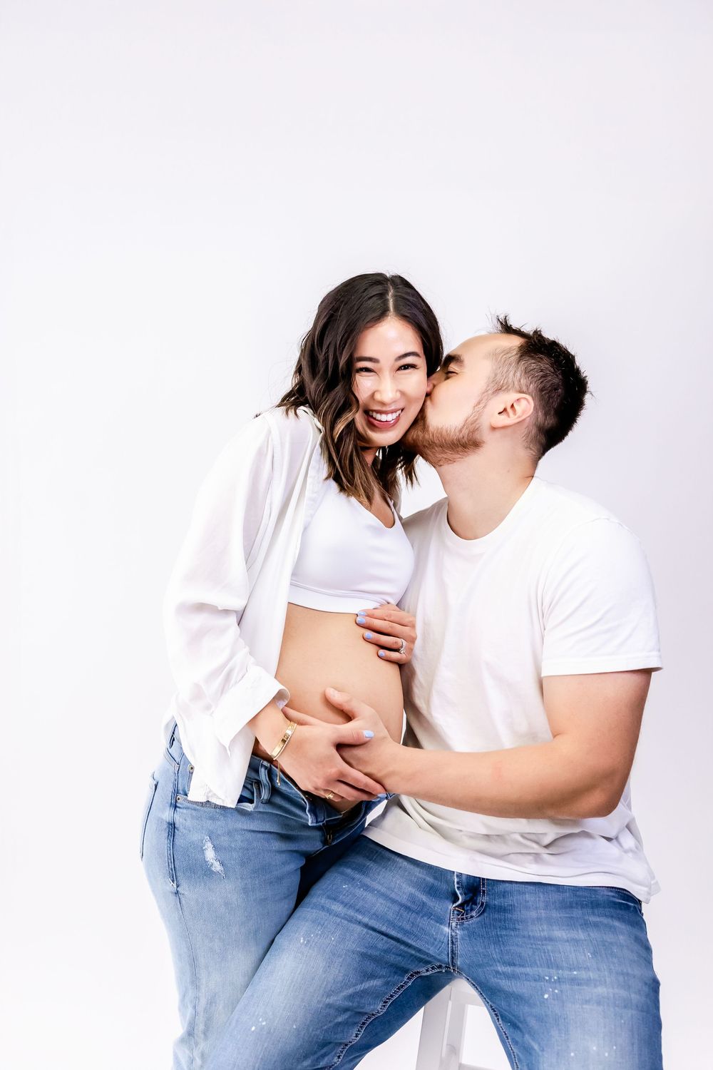 Couple in matching white tops and jeans sharing joyful moment against white backdrop.