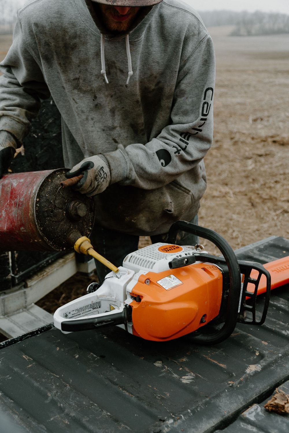 Person in gray hoodie maintaining a STIHL chainsaw on a truck bed.