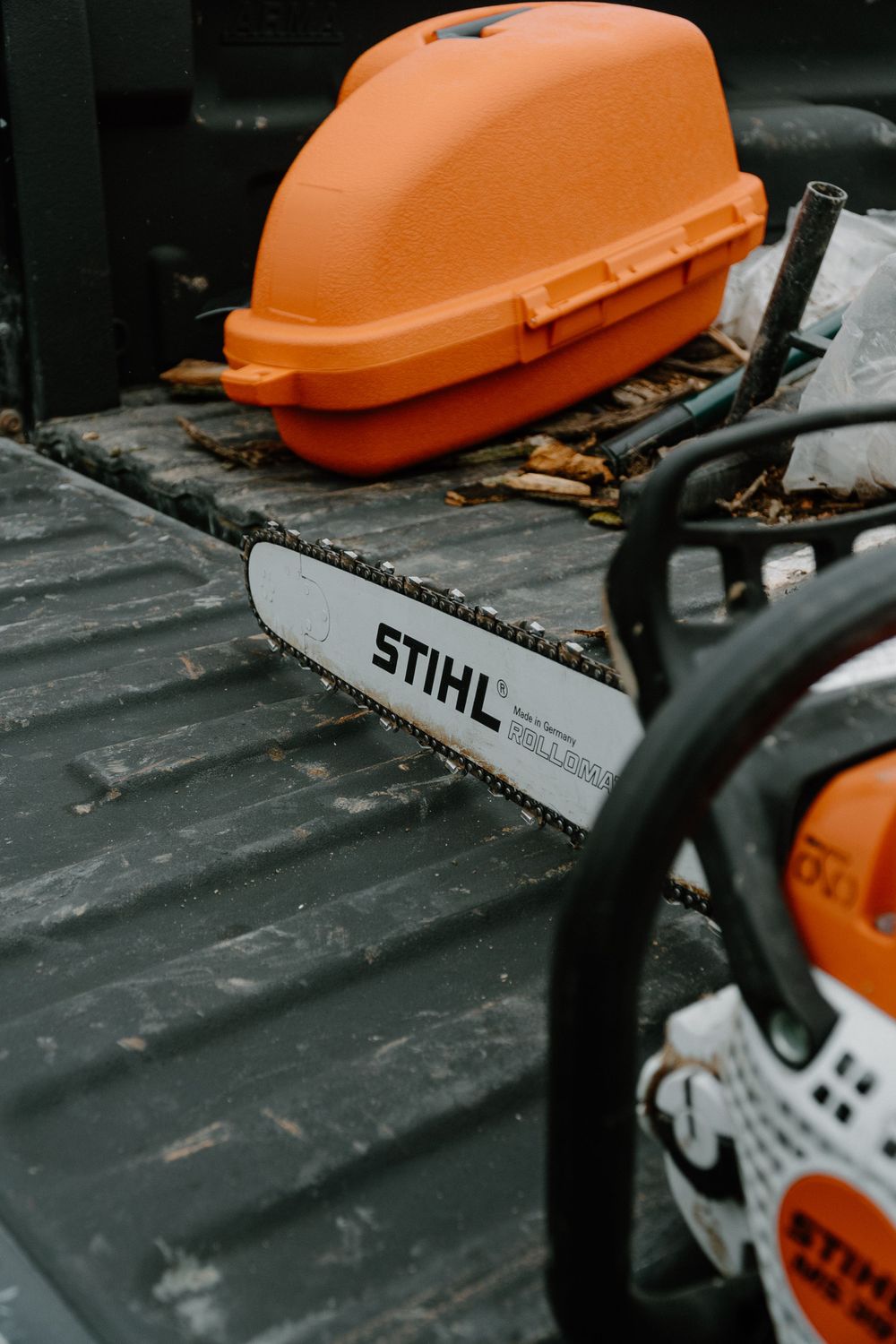 Orange STIHL chainsaw case and blade on black truck bed surface.