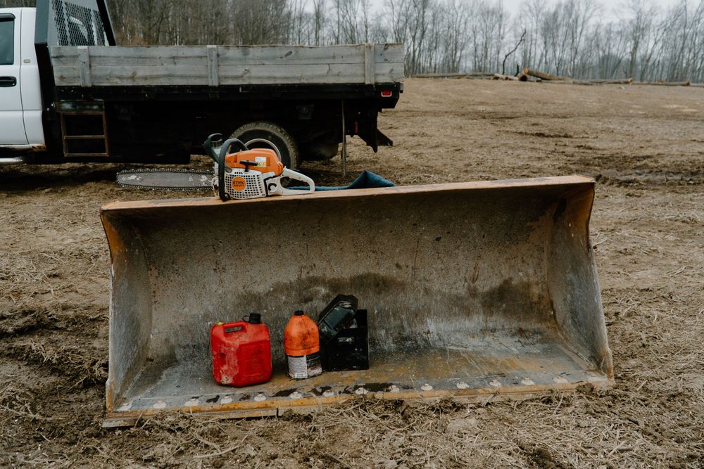 Chainsaw and fuel containers stored in rusty construction equipment bucket.