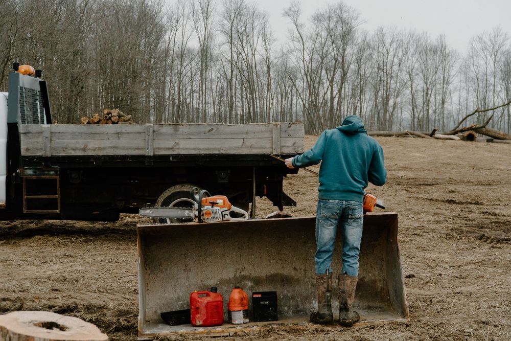 Person in work clothes standing by equipment on flatbed truck in rural setting.