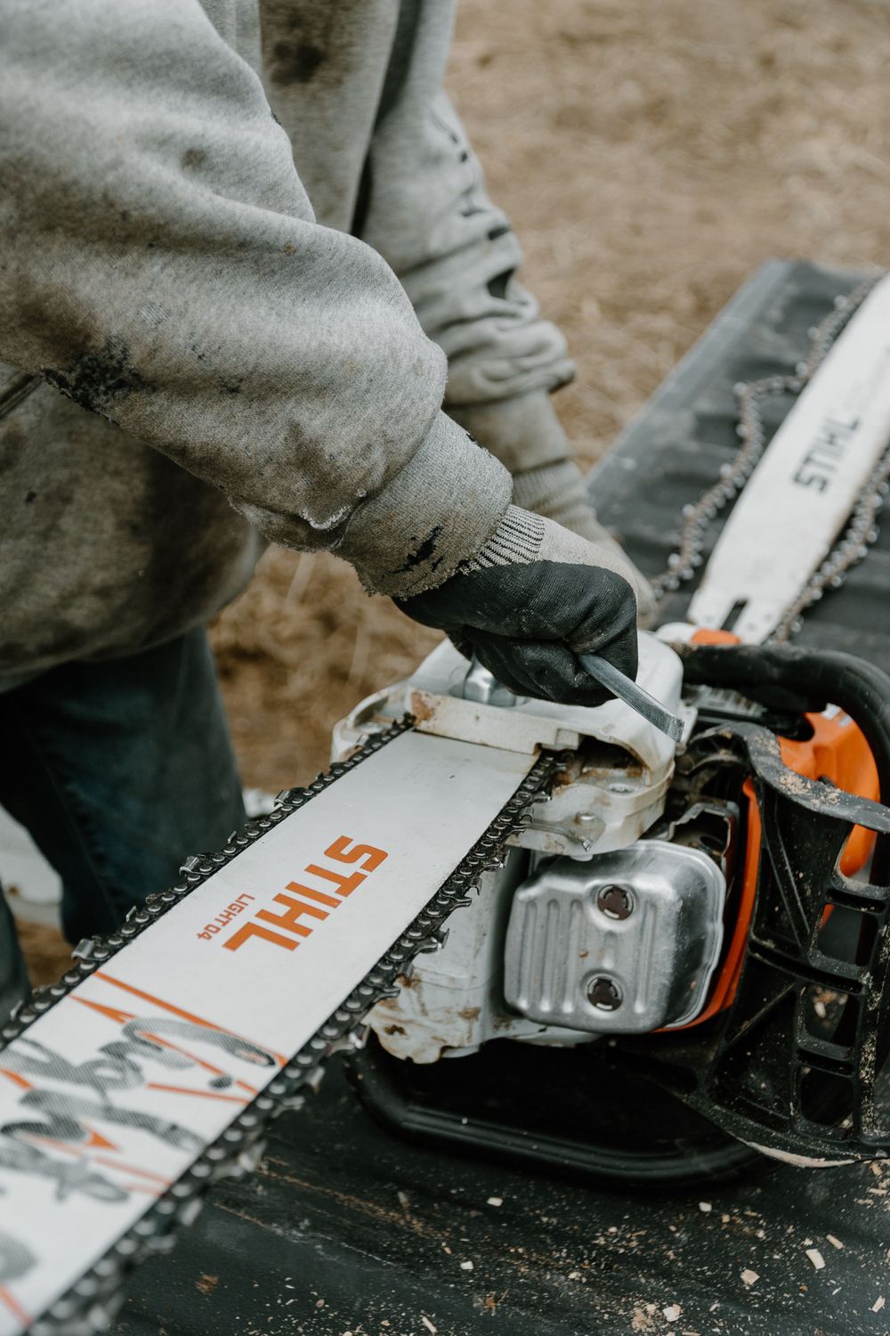 Close-up of hands adjusting a Stihl chainsaw chain on a work surface.
