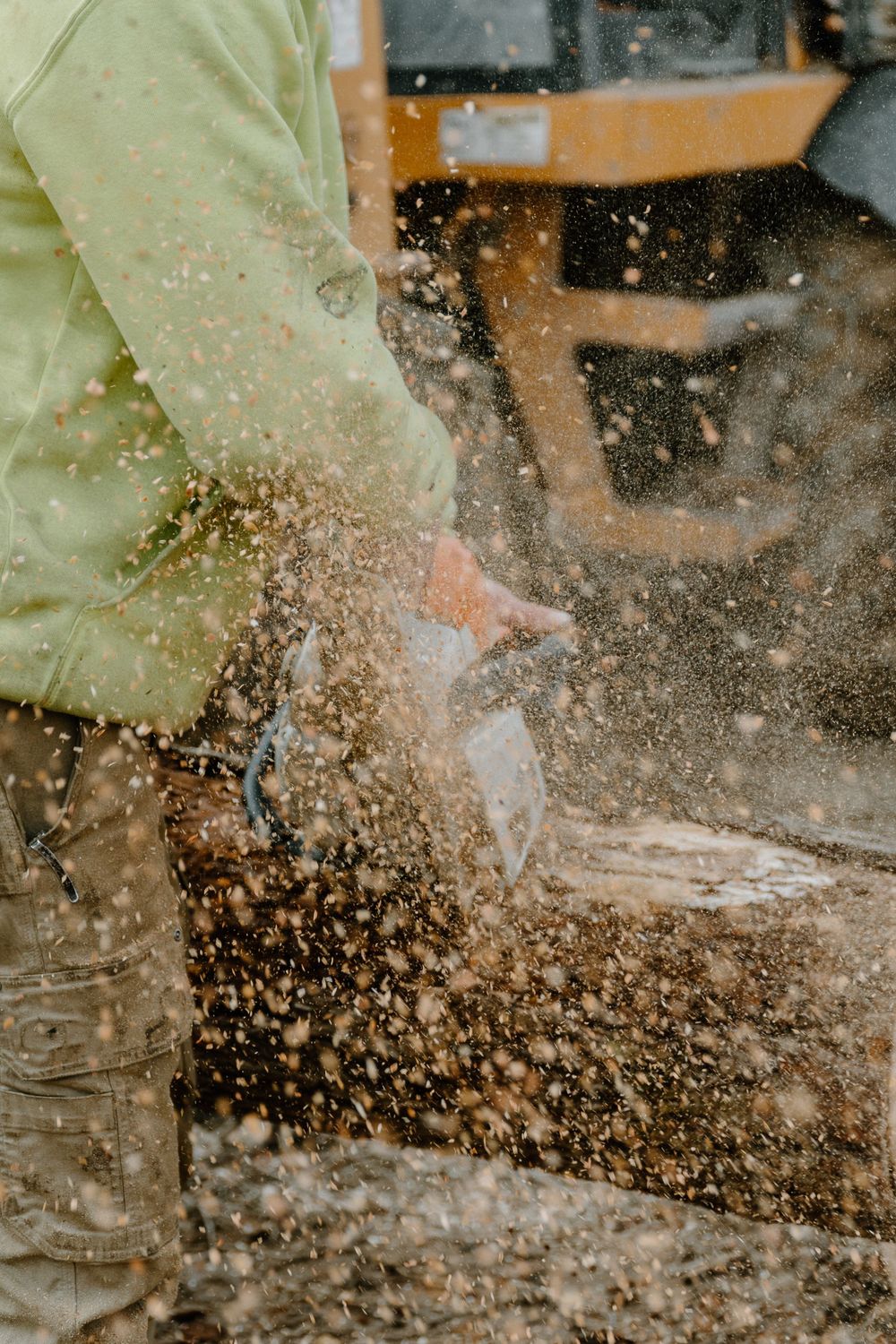 Sawdust spraying while chainsaw cuts through wood near heavy machinery.