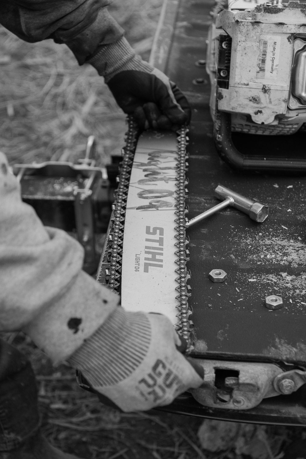 Detailed view of hands maintaining a chainsaw bar and chain in black and white.