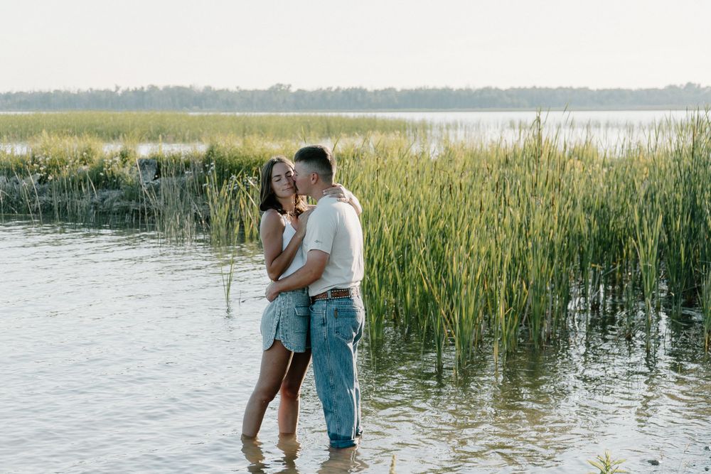 Romantic moment between couple standing in lake water with tall reeds in background.