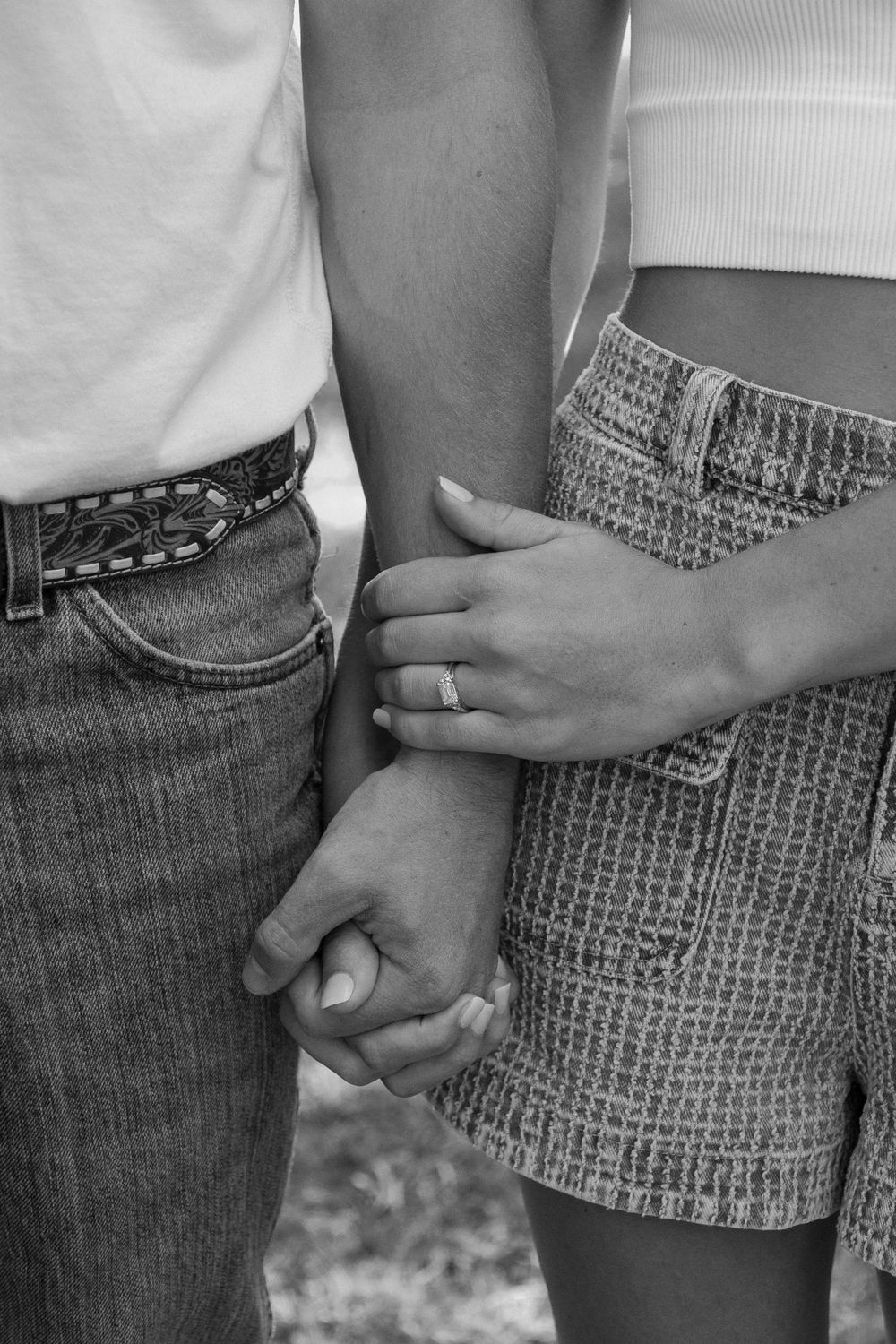 Black and white close-up of hands holding with engagement ring visible.