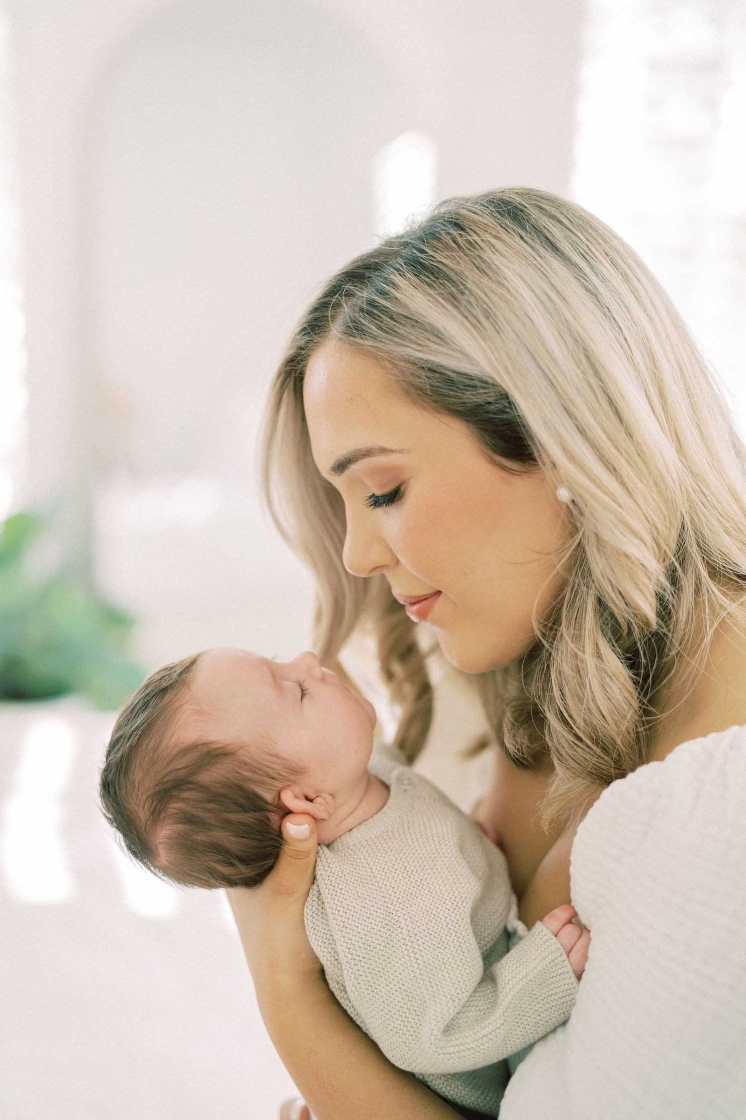 A tender moment between mother and newborn baby in soft natural light against a white background.