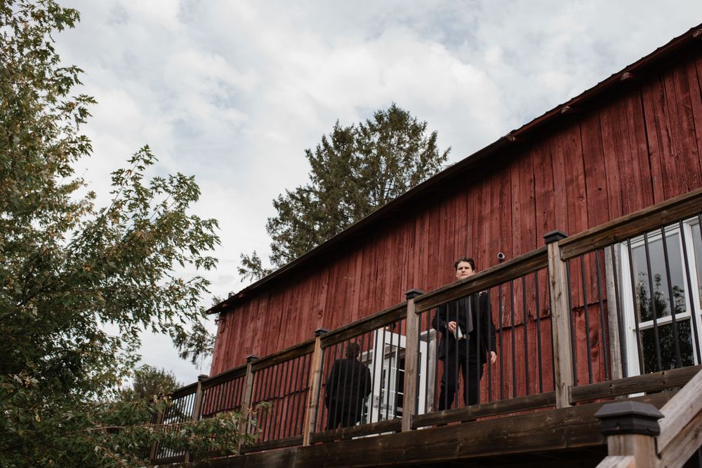 A rustic red wooden barn with weathered siding stands under cloudy skies, framed by autumn trees.