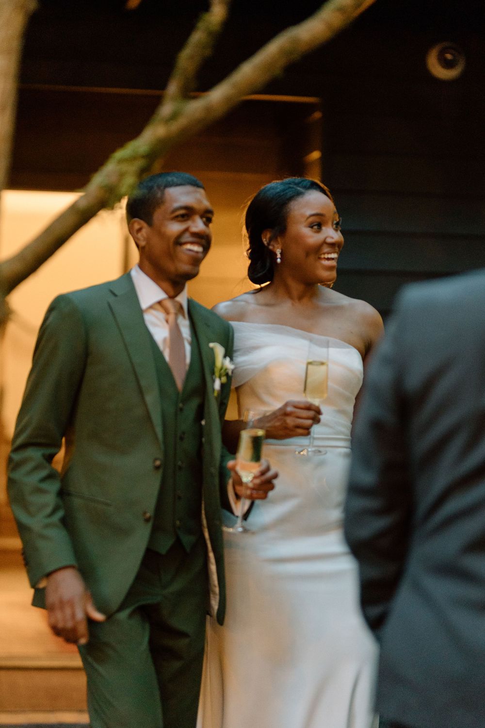 A newlywed couple shares a joyful moment during their wedding reception, dressed in an elegant green suit and white gown.