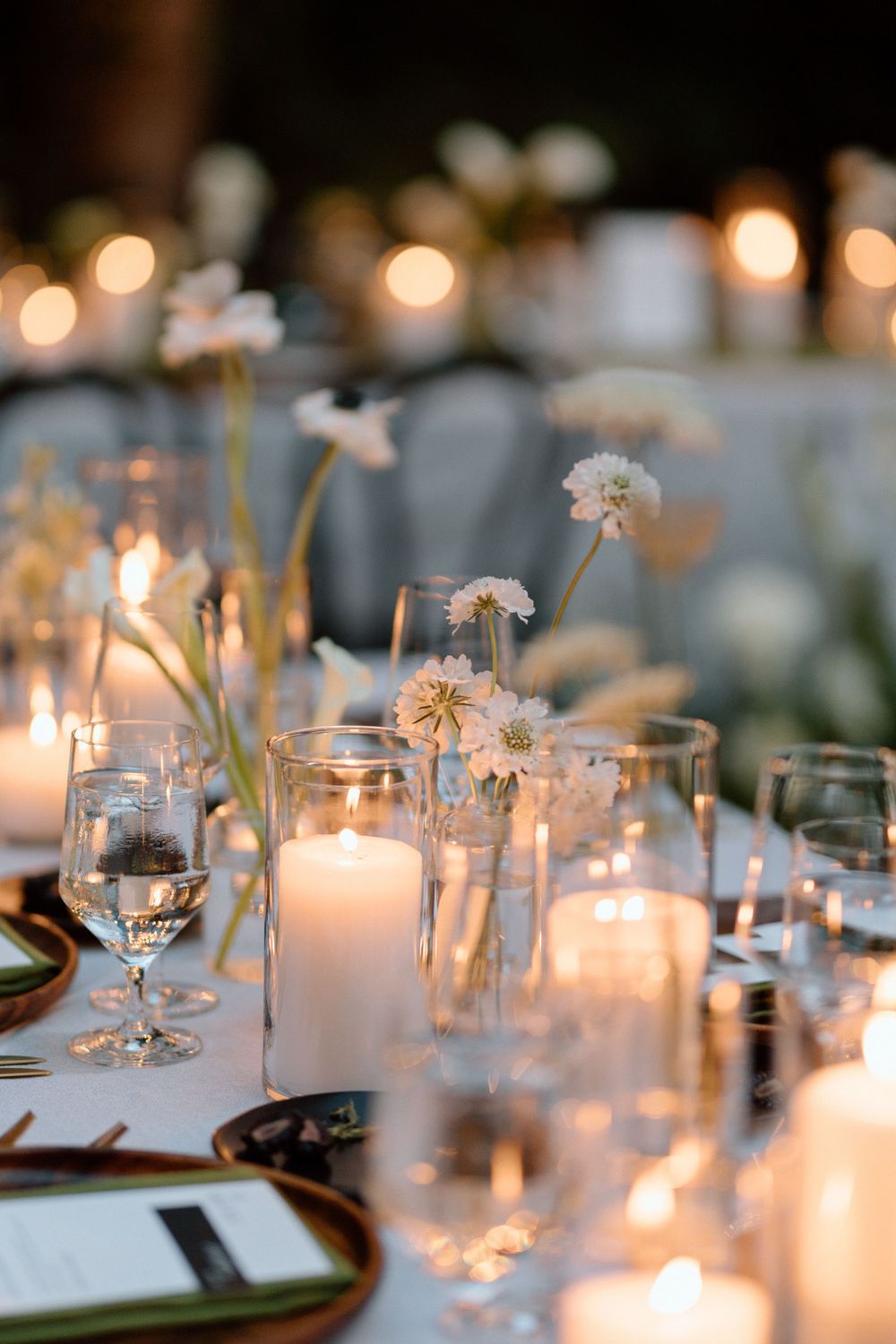 Elegant wedding table setting with glowing candles and delicate florals creating romantic ambiance at evening reception.