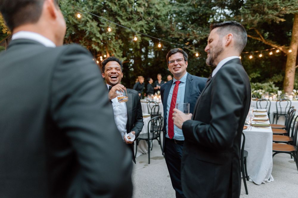 Guests in formal attire enjoying conversation at an outdoor wedding reception with garden setting and white decor.