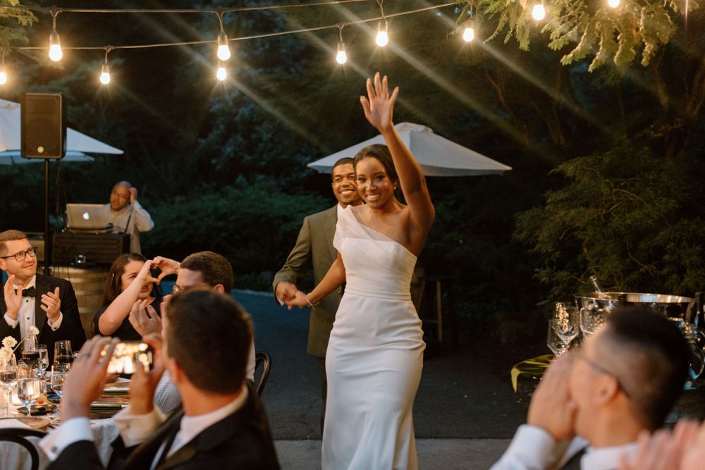 Evening outdoor wedding reception under string lights with joyful dancing during celebration.