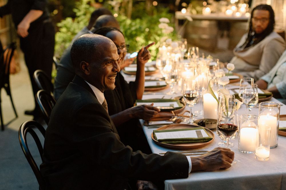 Guests enjoying an elegant candlelit outdoor dinner party with glowing candles and place settings on a white tablecloth.