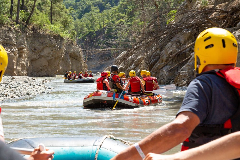 White water rafting adventure with multiple rafts navigating through rocky canyon walls on a sunny day.