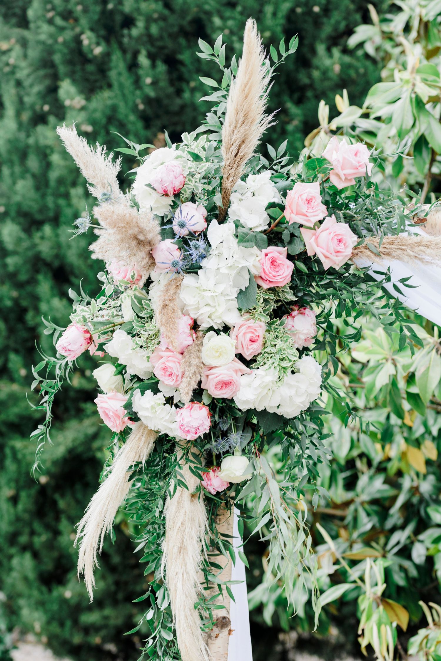Close-up of a lush floral arrangement with blush roses, white hydrangeas, eucalyptus, and pampas grass, decorating a wedding arch at Domaine