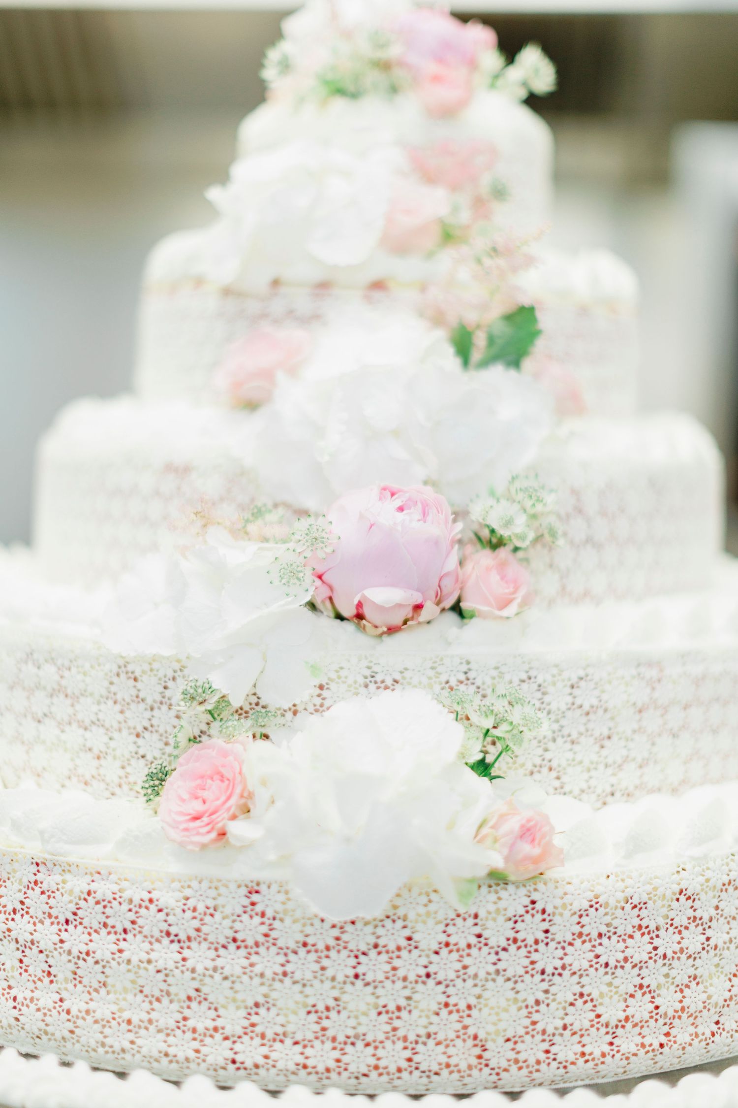 Elegant white tiered wedding cake decorated with delicate pink roses and lace pattern.