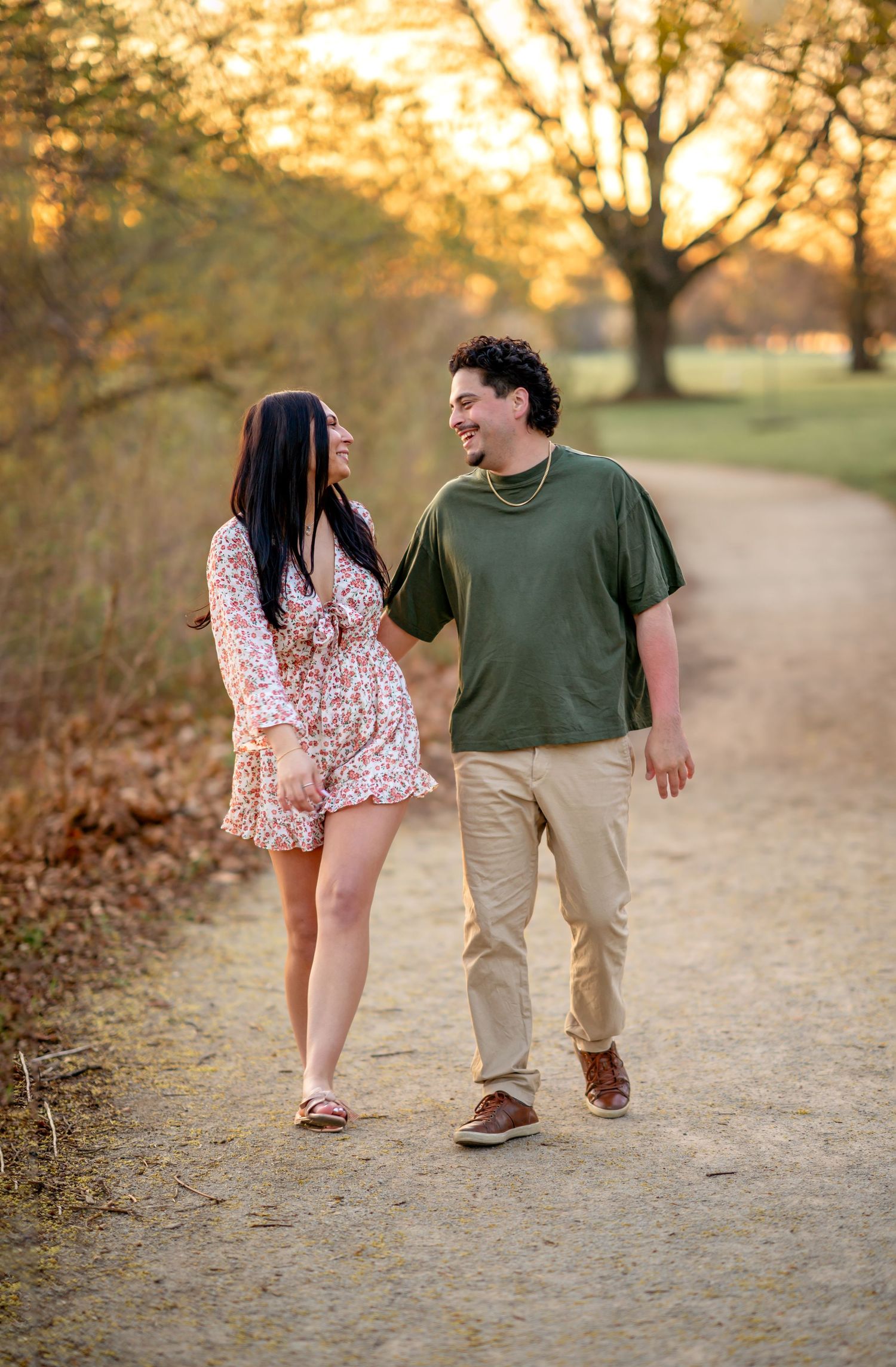 A couple walks together on a dirt path at sunset in a park during autumn.