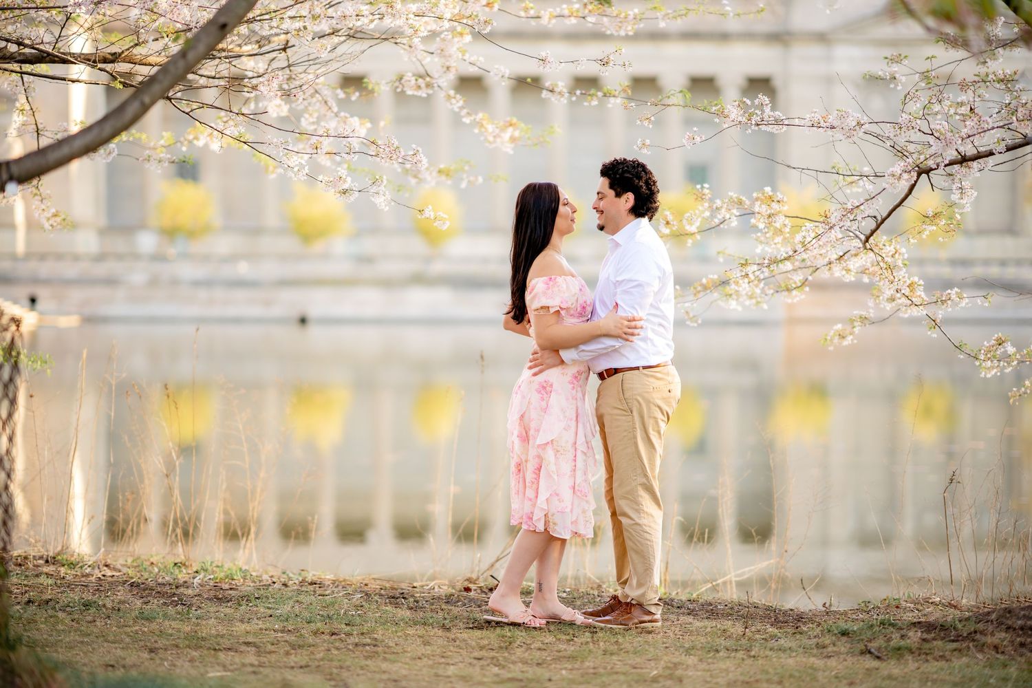 A couple embraces under blooming cherry blossoms with golden lanterns glowing in the soft evening light.