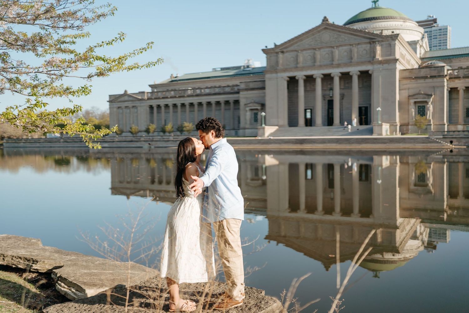 Couple embraces by tranquil lake with neoclassical Museum of Science and Industry reflected in water at Jackson Park Chicago.