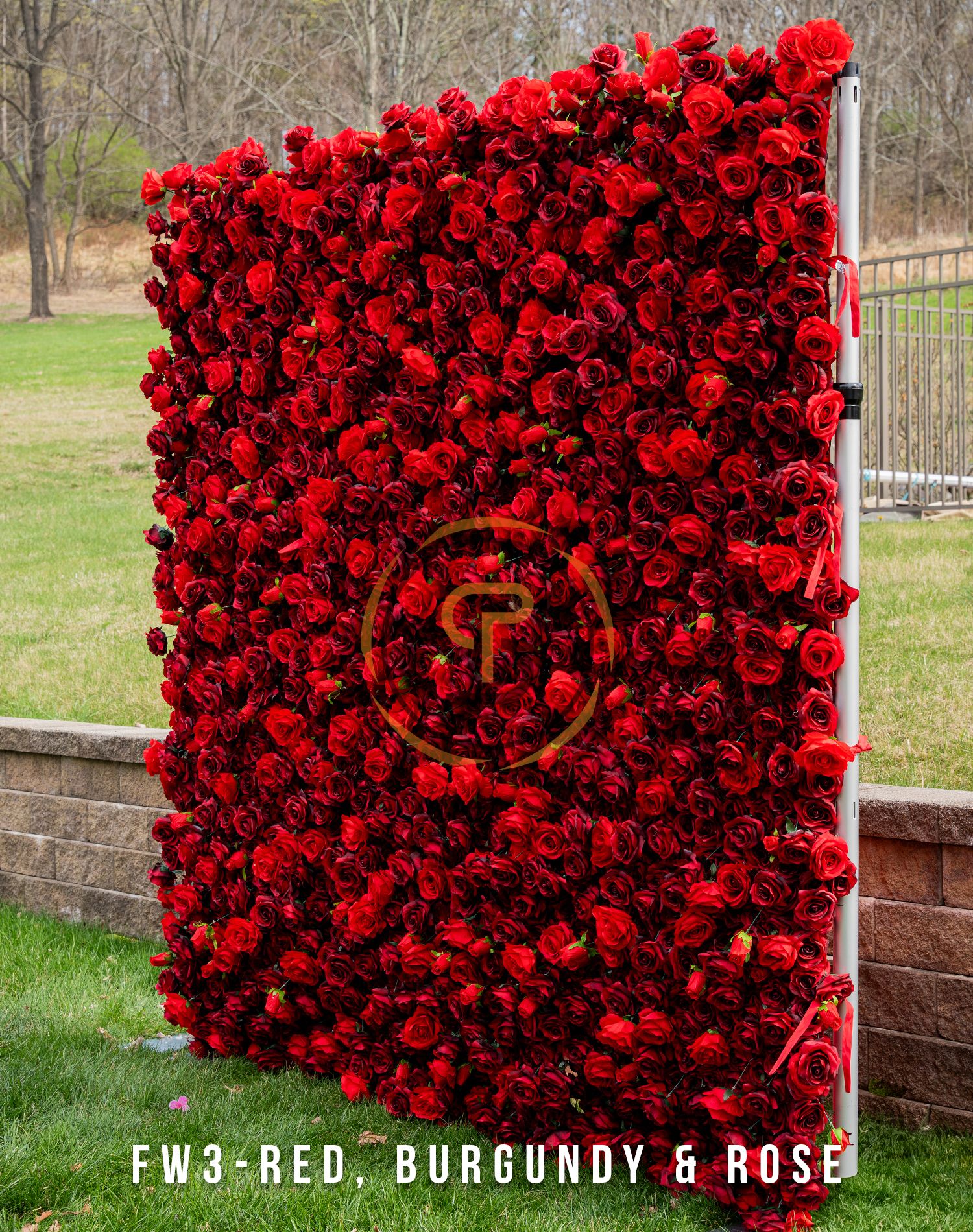 Deep red rose wall backdrop with monogram centerpiece against outdoor setting.