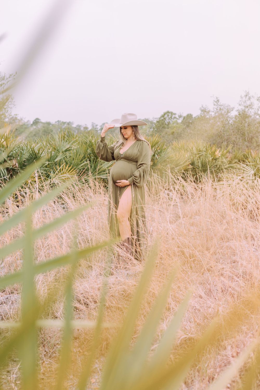 A serene figure walks through a golden sunlit field wearing a wide-brimmed hat and flowy dress.