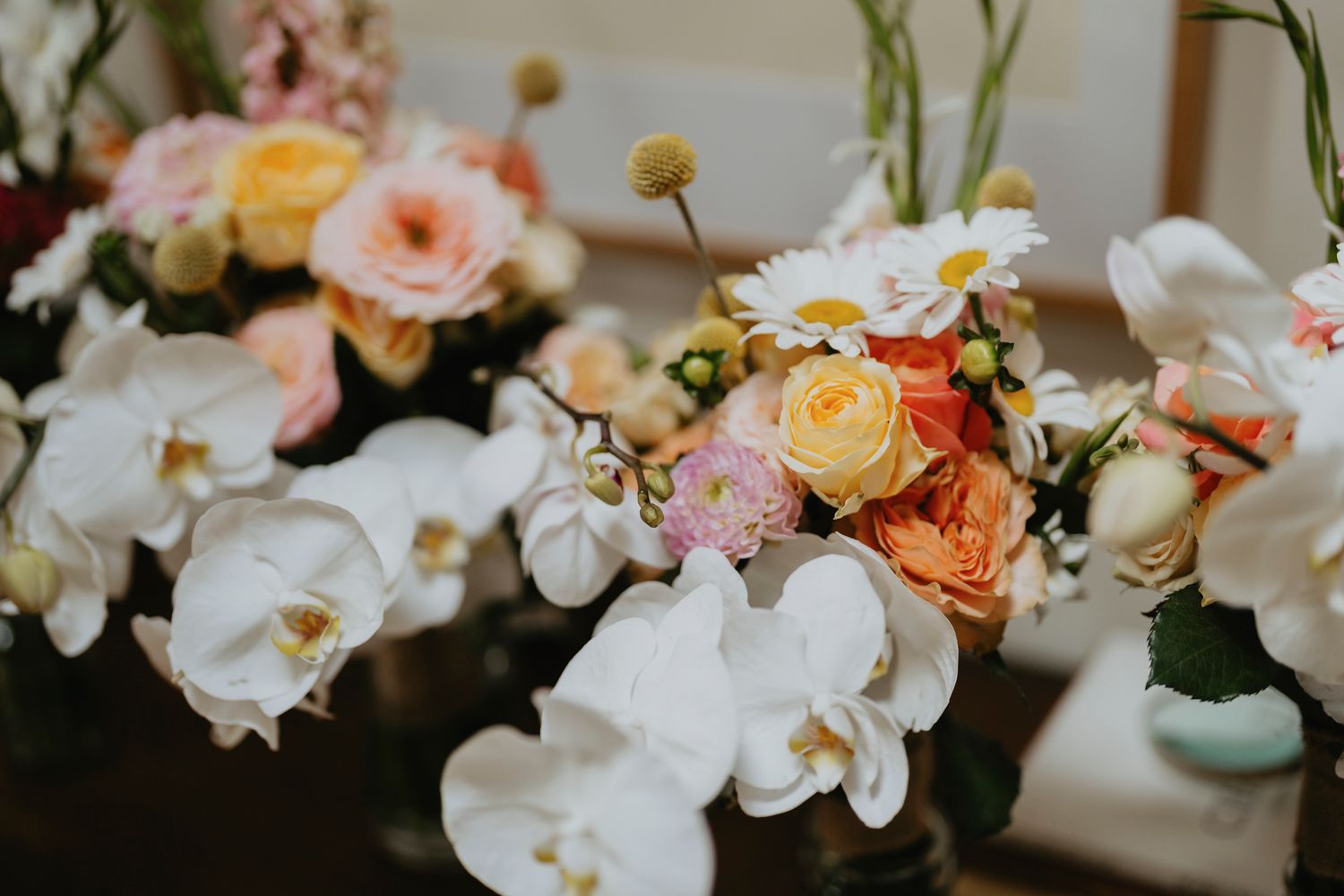 A beautiful floral arrangement featuring white orchids with peach and yellow roses on a dark surface.