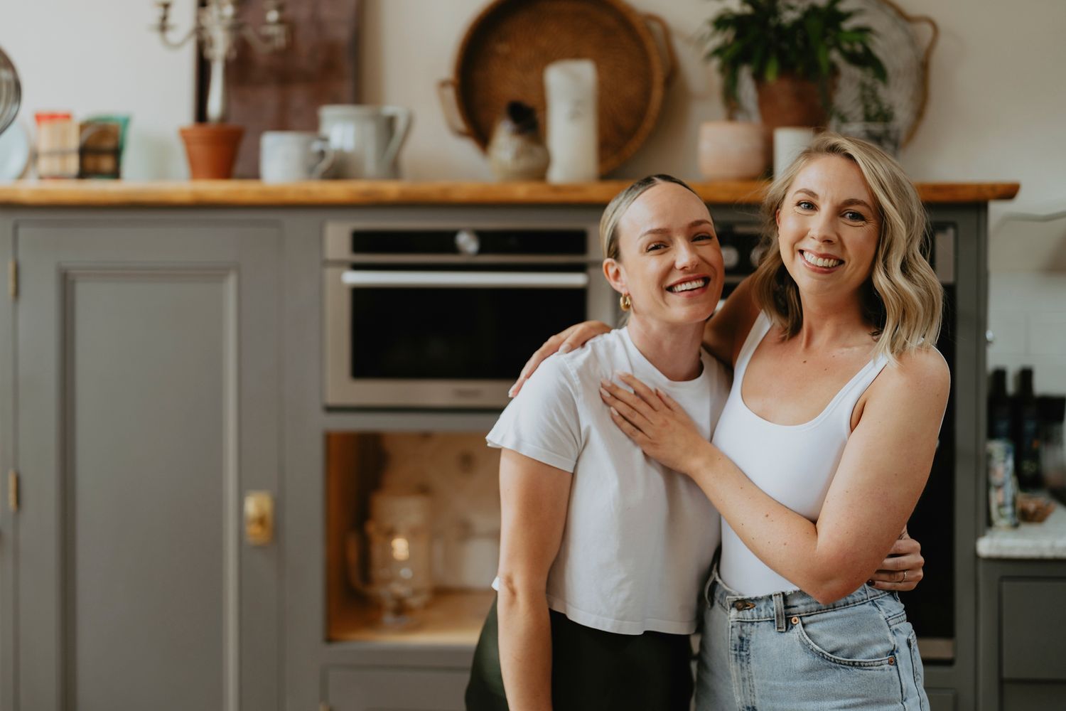 Two people share a joyful moment together while standing in a modern kitchen with gray cabinets and wooden shelving.
