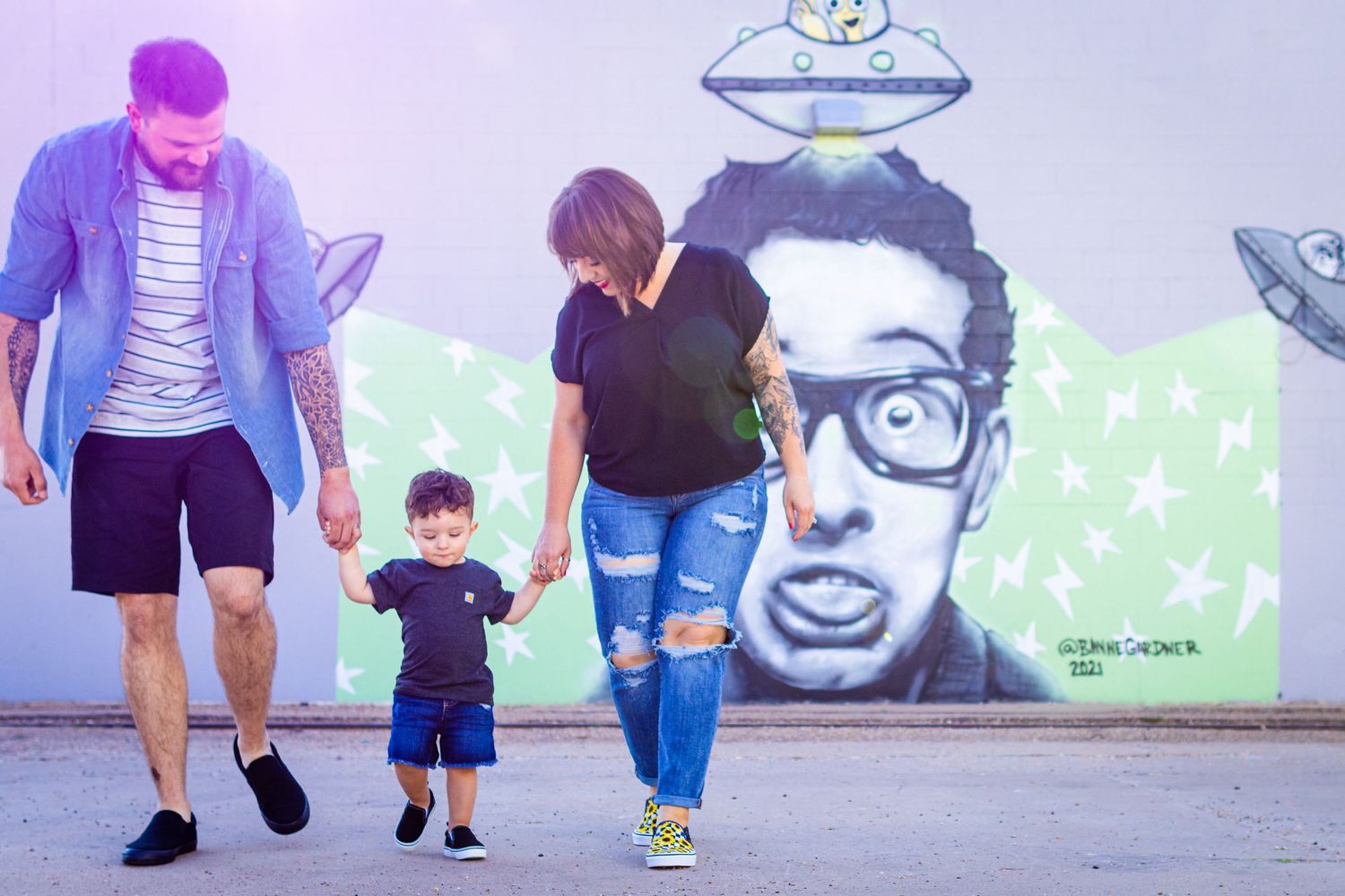 A parent and child walking together outdoors with colorful street art murals visible in the background.