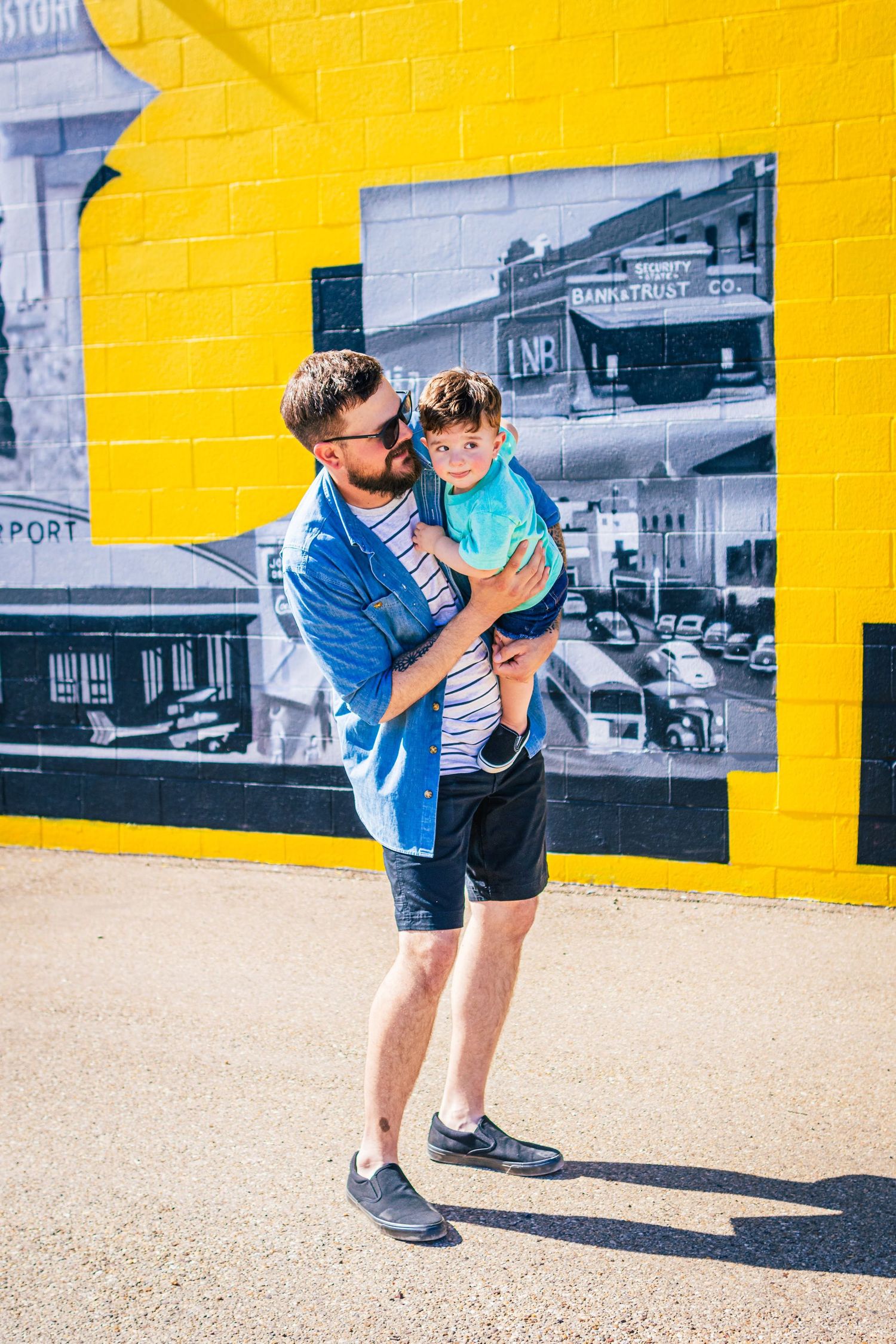 Parent and child playing together in front of a bright yellow wall with vintage black and white photographs.