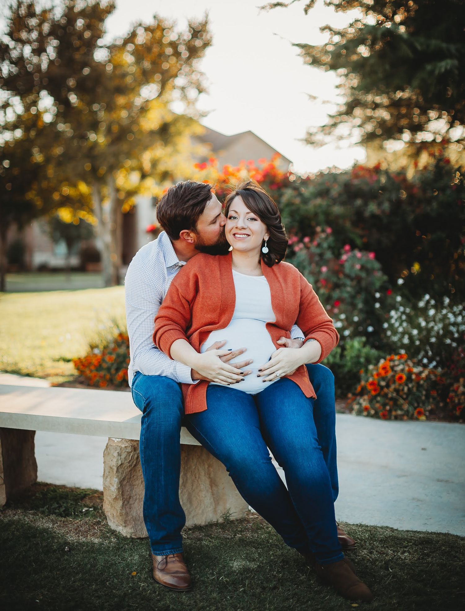 A couple sits close together on stone blocks at sunset surrounded by blooming flowers and trees.